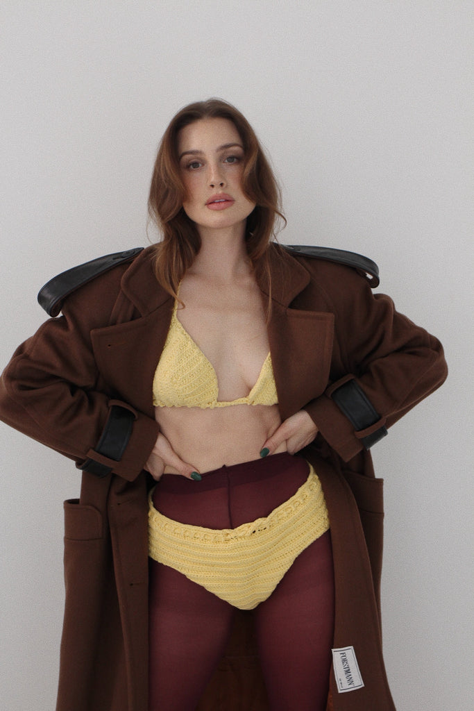 Woman wearing a yellow bikini and brown coat against a plain background