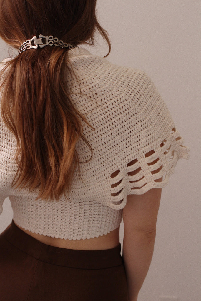 Person wearing a beige crochet top with a plain background